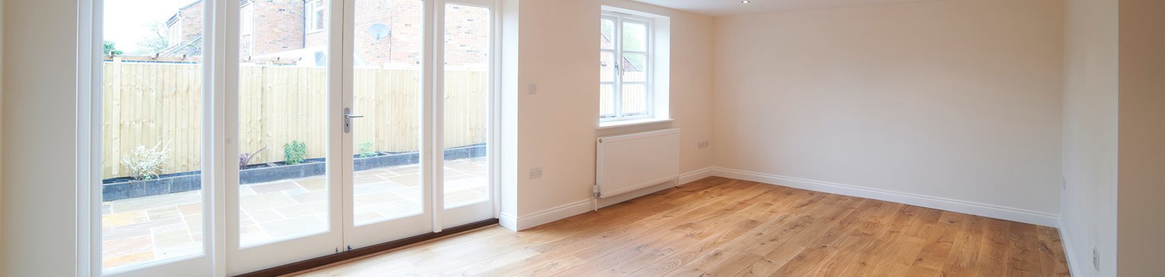 An empty room with wood floors, white walls, and large glass doors leading onto a brick patio.