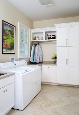A corner of a clean, well-designed laundry room with a washer and dryer on the left wall and white cabinets around a built-in clothes rack on the right wall.